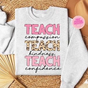 May include: A gray sweatshirt with the text "TEACH compassion TEACH kindness TEACH confidence" in pink lettering. The word "TEACH" in the middle is in a leopard print with pink hearts.