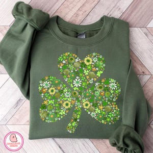 May include: Green sweatshirt featuring a floral shamrock design. The shamrock is composed of various green and yellow flowers. The sweatshirt is a solid green color, with the sleeves folded. The design is centered on the front of the sweatshirt.