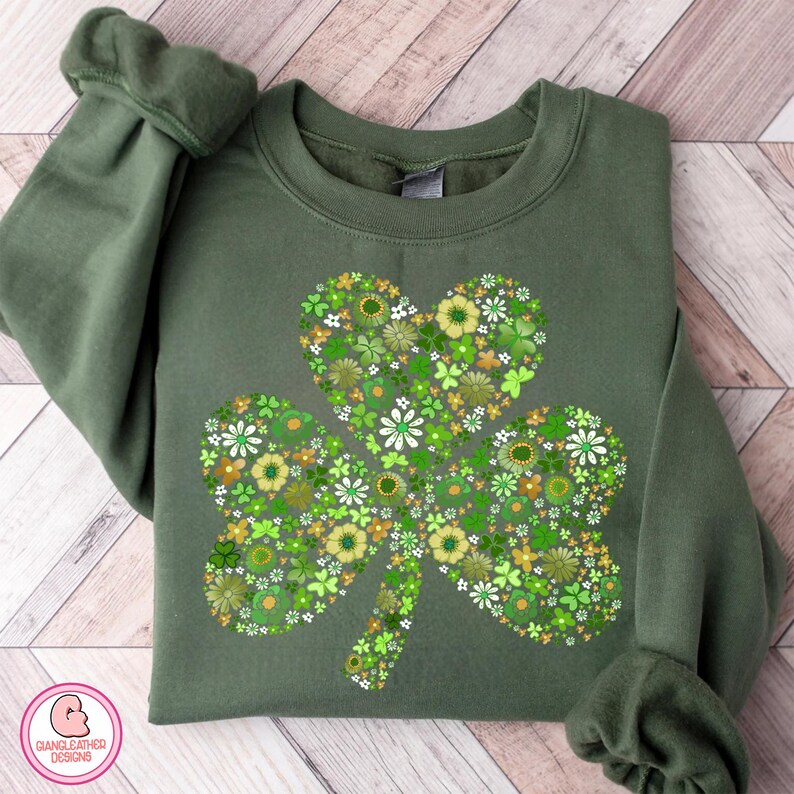 May include: Green sweatshirt featuring a floral shamrock design. The shamrock is composed of various green and yellow flowers. The sweatshirt is a solid green color, with the sleeves folded. The design is centered on the front of the sweatshirt.