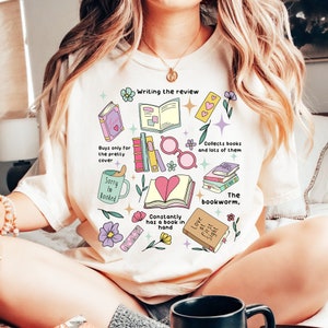 Op de afbeelding: Crèmekleurig T-shirt met een kleurrijke afbeelding van boeken, harten en leesgerelateerde zinnen. Het ontwerp bevat tekst als "Writing the review", "Sorry I'm Booked" en "Love at first sight". Het shirt heeft een relaxte pasvorm.