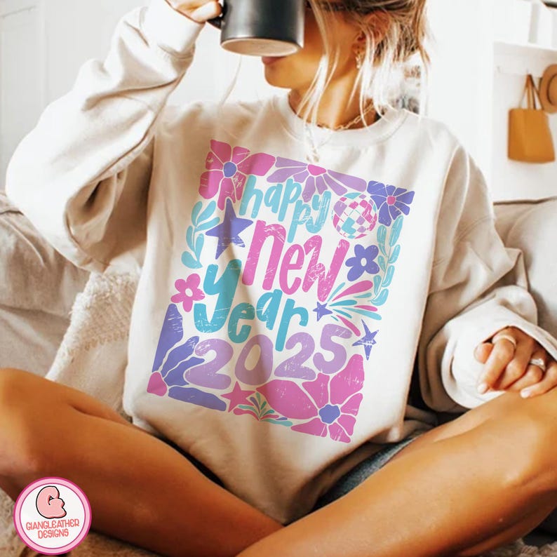 May include: A white sweatshirt with a colorful graphic design that says "Happy New Year 2025". The design features flowers, stars, and a disco ball.