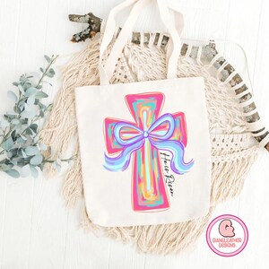 May include: A white canvas tote bag with a pink and blue cross with a blue bow and the text "He is Risen".