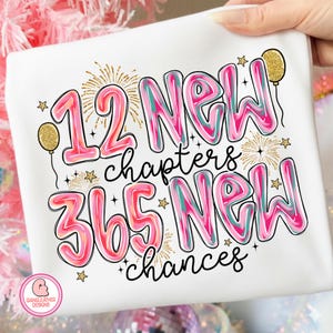 May include: White t-shirt with the text "12 New chapters 365 New chances" in pink, teal, and black. The design includes gold stars, fireworks, and balloons. A logo is in the bottom left corner.
