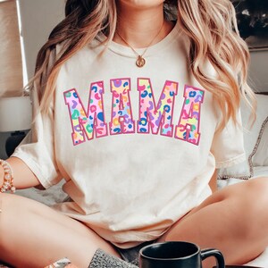 May include: A white t-shirt with the word "MAMA" printed in large, pink outlined letters. The letters are filled with a colorful leopard print pattern.