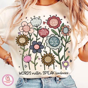 以下が含まれることがあります： クリーム色のTシャツ。花柄のデザインで、それぞれの花には「You are loved」や「I'm here for you」などのメッセージが書かれています。「WORDS matter SPEAK kindness」というテキストがTシャツの下部にあります。