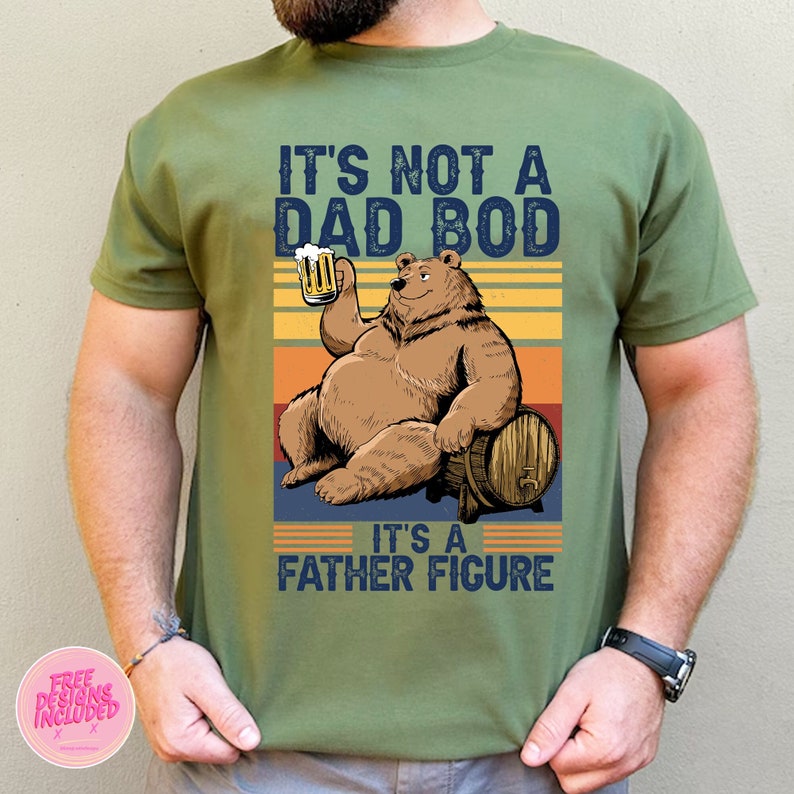 May include: A green t-shirt with a vintage-style graphic of a bear holding a beer and sitting on a barrel. The text on the shirt reads "It's not a dad bod, it's a father figure."