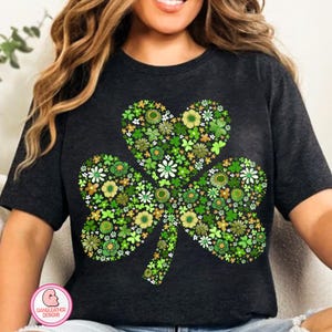 May include: Dark gray t-shirt featuring a floral shamrock design. The shamrock is composed of various green and white flowers and leaves, with a heart-shaped top leaf. A St. Patrick's Day themed graphic tee.