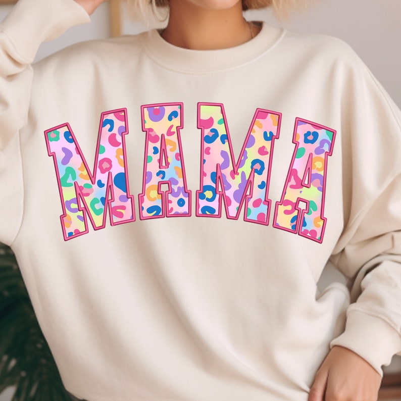 May include: A cream colored sweatshirt with the word "MAMA" printed in large, pink outlined letters. The letters are filled with a colorful leopard print pattern.