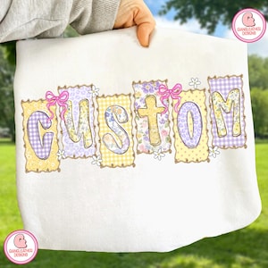 May include: White fabric with the word "CUSTOM" in colorful, patterned letters. Each letter is a different design, including floral, gingham, and leopard print. Pink bows and small white flowers accent the letters.