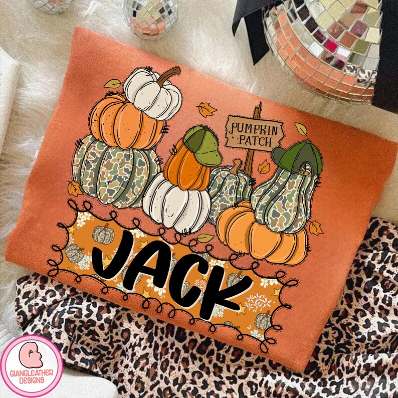 May include: Orange long-sleeve shirt with a pumpkin patch design. The design features stacks of pumpkins in orange, white, and camouflage green, with the name "JACK" in large black letters. A sign reads "Pumpkin Patch".