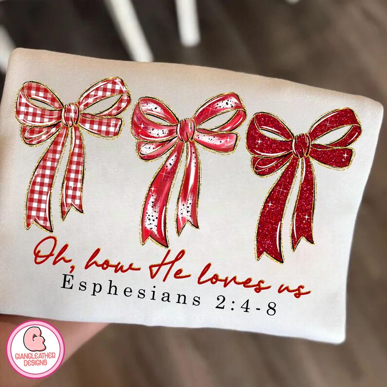 May include: Cream-colored t-shirt featuring three red bows with gold trim. The bows have varying designs, including gingham and glitter. The text "Oh, how He loves us" and "Ephesians 2:4-8" are printed in red script.