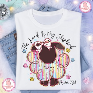 May include: White t-shirt with a cartoon sheep design. The sheep has a bow and colourful stripes. The text "The Lord Is My Shepherd" and "Psalm 23:1" are printed on the shirt. The design includes pink, blue, yellow, and gold accents.