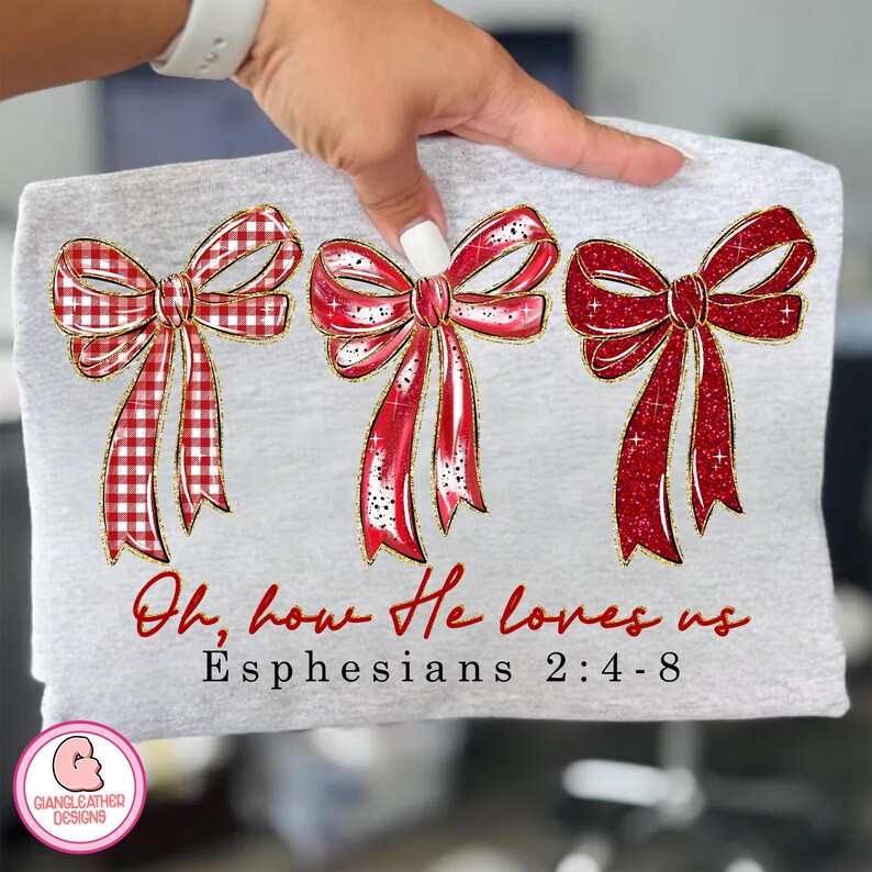 May include: A light gray t-shirt featuring three red bows with gold trim. The bows have a mix of solid and plaid patterns. The text "Oh, how He loves us" and "Ephesians 2:4-8" are printed in red script.