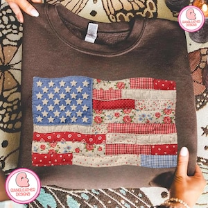 Peut inclure: Un sweat-shirt marron orné d'un drapeau américain en patchwork. Le drapeau comprend un tissu bleu avec des étoiles blanches et des sections rayées rouges et blanches avec des motifs floraux et vichy. Le sweat-shirt est présenté sur une surface à motifs.