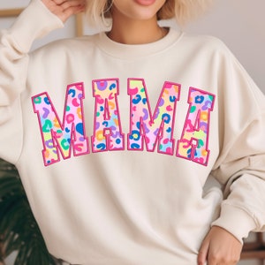 May include: A cream-colored sweatshirt with the word "MAMA" printed in large, pink outlined letters. The letters are filled with a colorful leopard print pattern.
