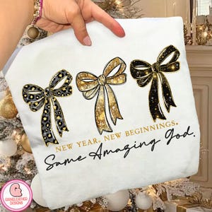 May include: White fleece blanket featuring three decorative bows in gold, black, and leopard print. The text "NEW YEAR. NEW BEGINNINGS. Same Amazing God." is printed in black and gold.