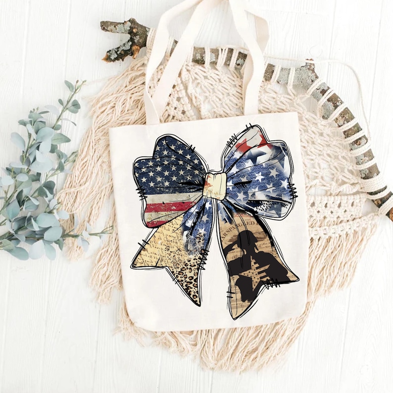 May include: A white tote bag with a large, distressed, red, white, and blue bow. The bow is made of fabric with a stars and stripes pattern. The bow is tied with a white ribbon. The bow is centered on the bag. The bag has a white background.