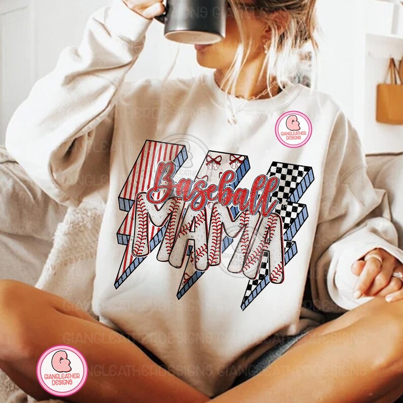 May include: White sweatshirt with a graphic that says "Baseball Mama" in red script and baseball-themed lightning bolt designs. The lightning bolts have red and white stripes, baseball stitching, and a black and white checkered pattern.