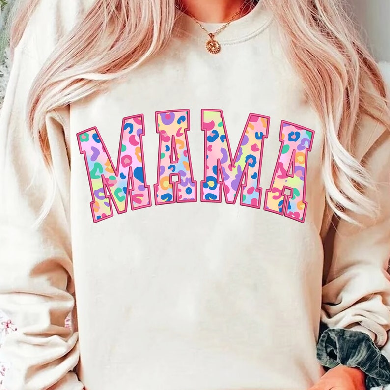 May include: A cream colored sweatshirt with the word "MAMA" printed in large, pink outlined letters. The letters are filled with a colorful leopard print pattern.