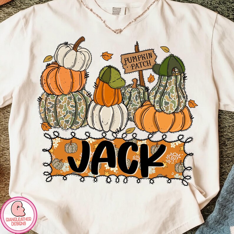 May include: Cream-colored t-shirt featuring a fall-themed graphic. The design includes stacked pumpkins in orange, white, and camouflage patterns, some wearing hats. The word "JACK" is displayed in a decorative frame, with a "PUMPKIN PATCH" sign.