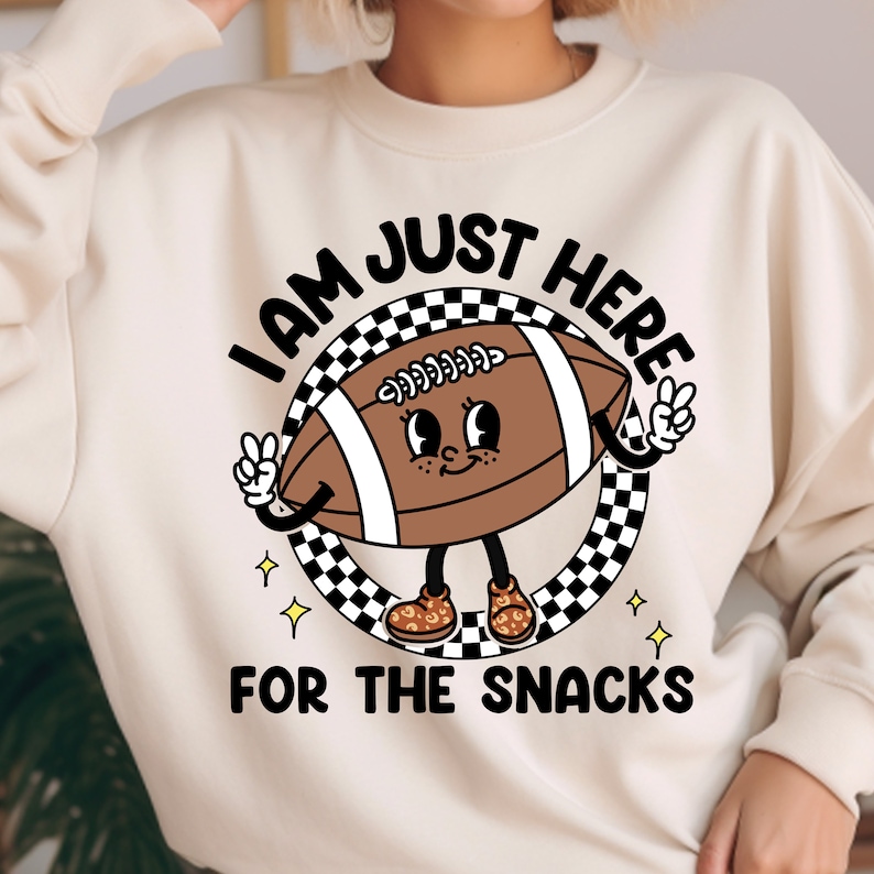May include: A white sweatshirt with a cartoon football character wearing sneakers and the text "I am just here for the snacks".