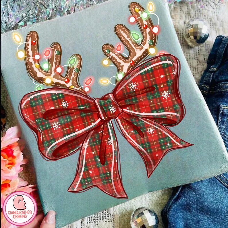 Puede incluir: Un coj&iacute;n decorativo azul claro con un dise&ntilde;o navide&ntilde;o. El dise&ntilde;o incluye cuernos de reno de pan de jengibre adornados con luces de cadena y un gran lazo a cuadros rojo con copos de nieve blancos. El coj&iacute;n tiene el texto "GIANGLEATHER DESIGNS".