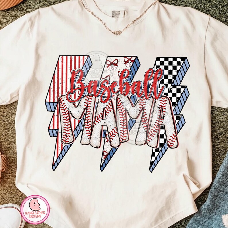 May include: Cream-colored t-shirt with a baseball-themed design. The design features the words "Baseball MAMA" in red script and baseball stitching, set against lightning bolt shapes with red, white, blue, and black patterns.