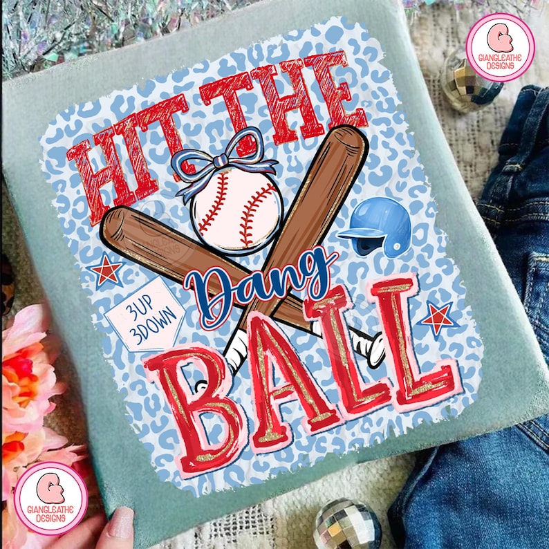 May include: A light blue baseball-themed t-shirt with the words "HIT THE BALL" in red, a baseball, crossed bats, and a blue helmet. The design includes the word "Dang" and the phrase "3 UP 3 DOWN".