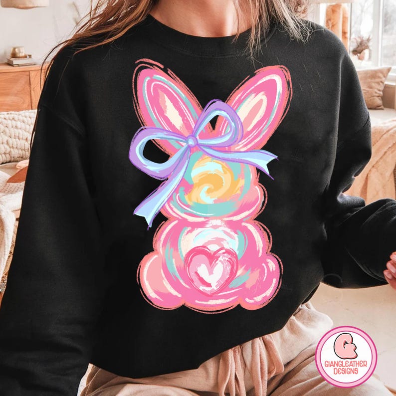 May include: Black sweatshirt with a colorful abstract bunny design. The bunny has a large pink bow with a blue ribbon.
