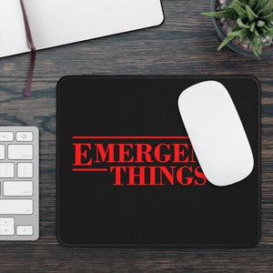 May include: Black mouse pad with red text that reads "Stranger Things" with a white computer mouse on top of it.