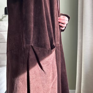 May include: A long brown suede coat with a tie closure and a large pocket on the front.