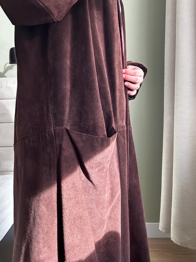 May include: A long brown suede coat with a tie closure and a large pocket on the front.