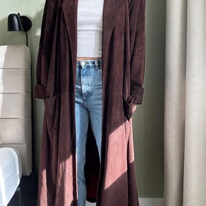 May include: A long brown suede coat with a collar and pockets.