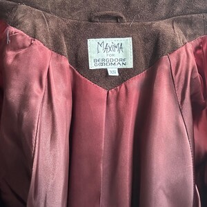 May include: A brown suede jacket with a burgundy lining. The jacket has a label that reads "Maxima for Bergdorf Goodman" and "XS".