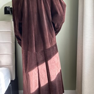 May include: A long brown suede coat with a collar and long sleeves.