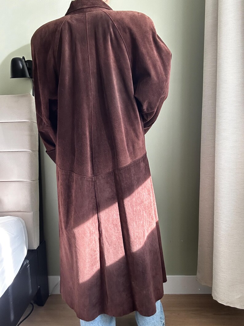 May include: A long brown suede coat with a collar and long sleeves.