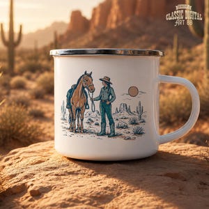 May include: White enamel mug with a silver rim featuring a Western-themed illustration. The design depicts a person with a horse in a desert landscape with cacti and a setting sun. The mug has a large, curved handle.