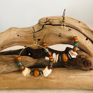 May include: A pair of gold hoop earrings with wooden and shell beads. The beads are in shades of brown, white, and turquoise.