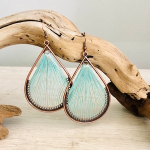 May include: A pair of teardrop-shaped earrings with a copper wire frame and a light blue thread design.