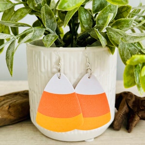 May include: A pair of dangle earrings shaped like candy corn. The earrings are white, orange, and yellow. The earrings are hanging from silver hooks.