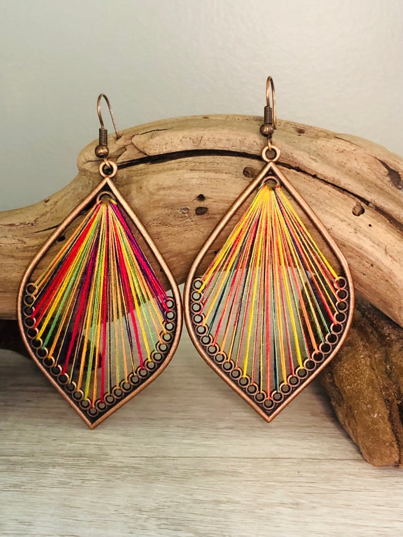 May include: A pair of colourful, teardrop-shaped earrings with a copper wire frame and a woven design of multi-coloured threads.