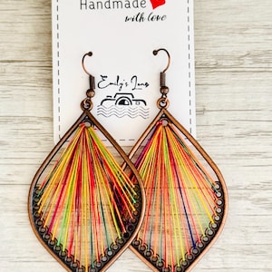 May include: A pair of handmade earrings in a teardrop shape. The earrings are made from copper wire and feature a colourful thread design. The earrings are labelled "Handmade with love".