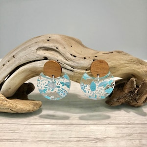 May include: A pair of blue and white resin earrings with a wood accent. The earrings feature a sea turtle design.