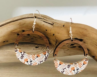 May include: A pair of wooden earrings with a floral pattern. The earrings are shaped like half circles and have a silver hook.