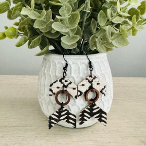 May include: A pair of black and white geometric patterned wood earrings with wooden rings hanging from them.