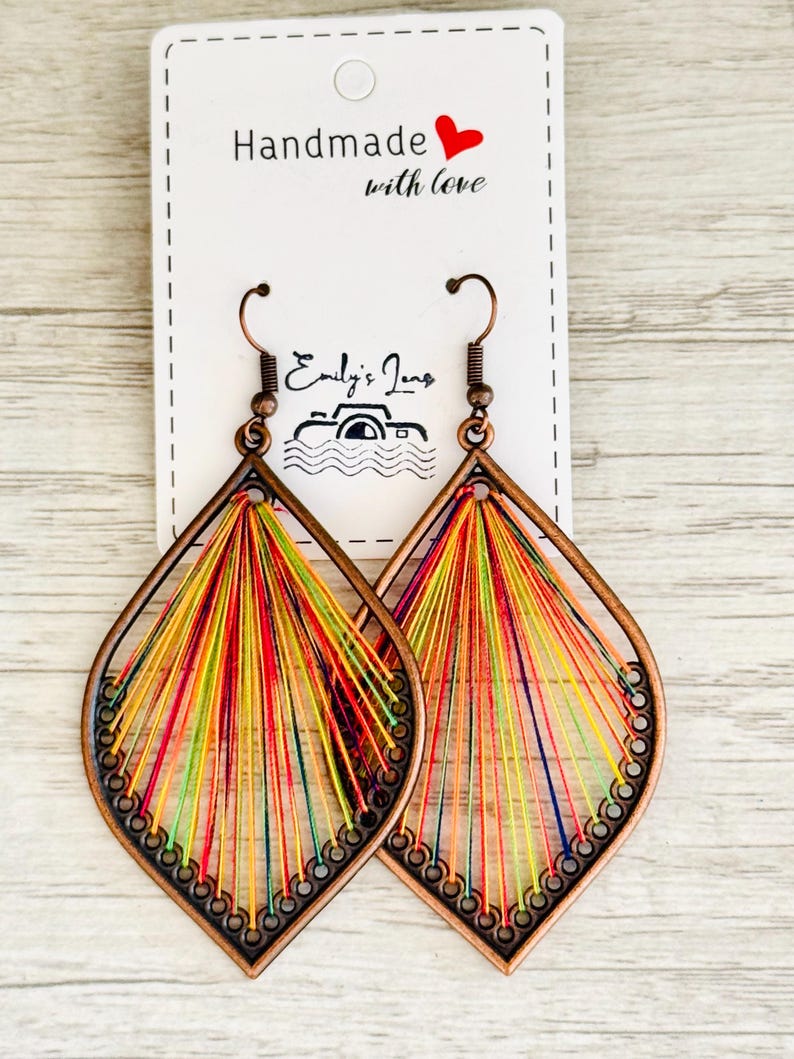 May include: A pair of handmade earrings in a teardrop shape. The earrings are made from copper wire and feature a colourful thread design. The earrings are labelled "Handmade with love".