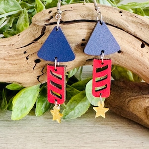 May include: A pair of dangle earrings with a red and blue color scheme. The earrings feature a blue triangle, a red rectangle with white stripes, and a gold star charm.