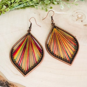 May include: A pair of teardrop-shaped earrings with a copper frame and colourful thread woven into a radial pattern.