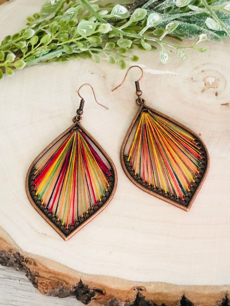 May include: A pair of teardrop-shaped earrings with a copper frame and colourful thread woven into a radial pattern.