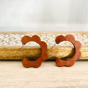 May include: A pair of brown wooden hoop earrings with a scalloped edge.